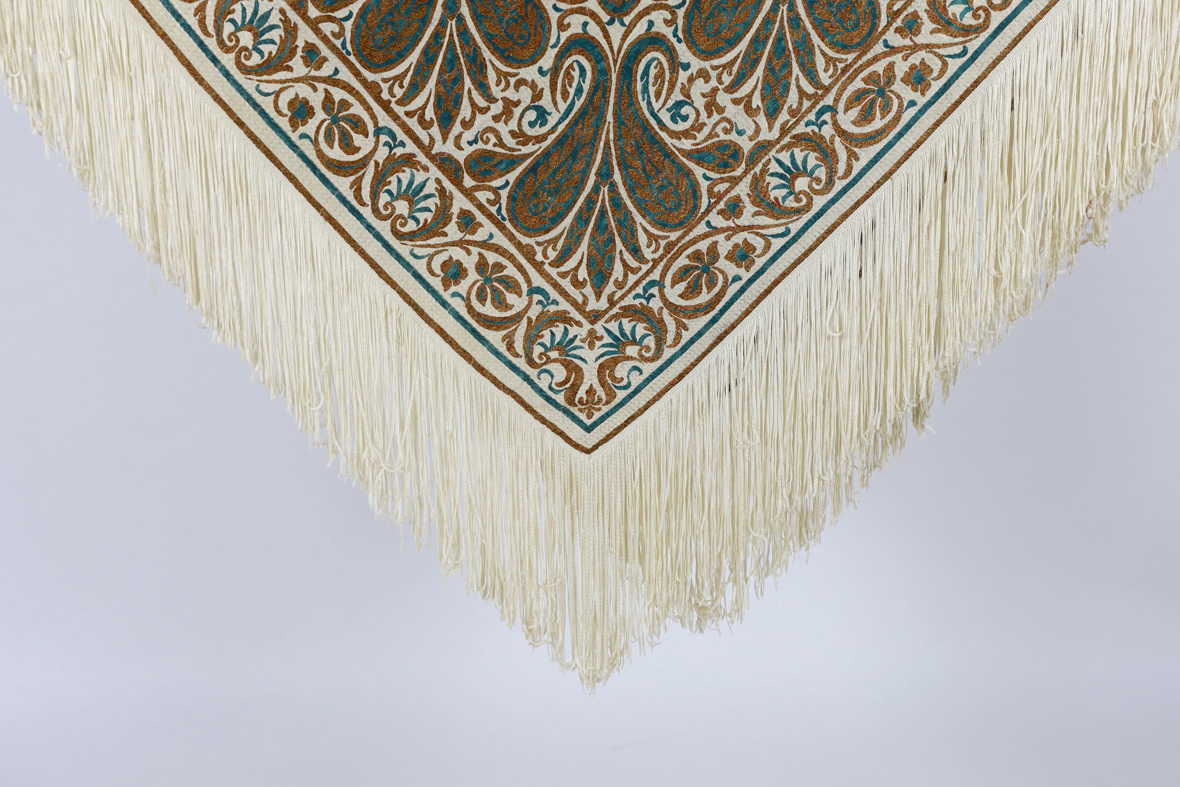 A 1920’s-1930’s cream silk woven shawl, woven with turquoise and bronze coloured silks in an all over tear drop paisley motif, edged with fine knitted cream fringing, approximately 109cm x 120cm